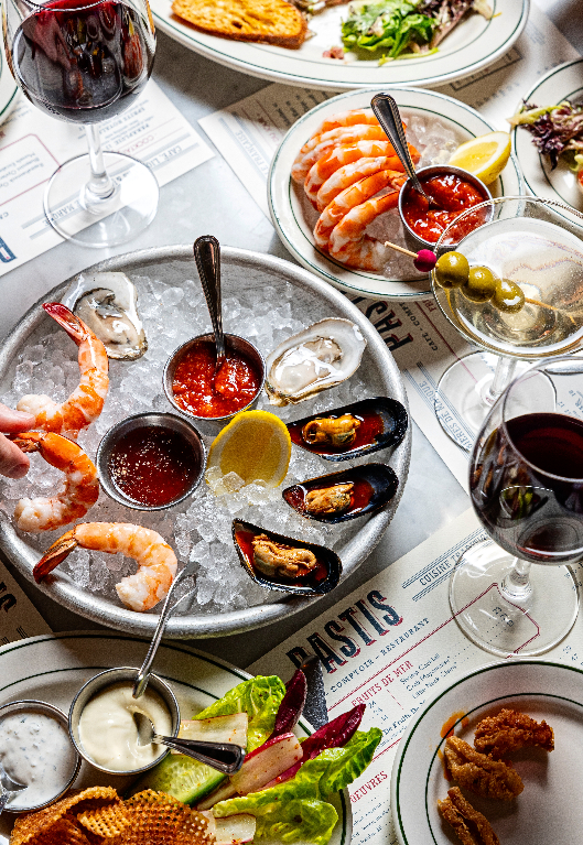 Seafood platter with shrimp, oysters, and mussels on ice with cocktail sauce, served alongside wine glasses and appetizers