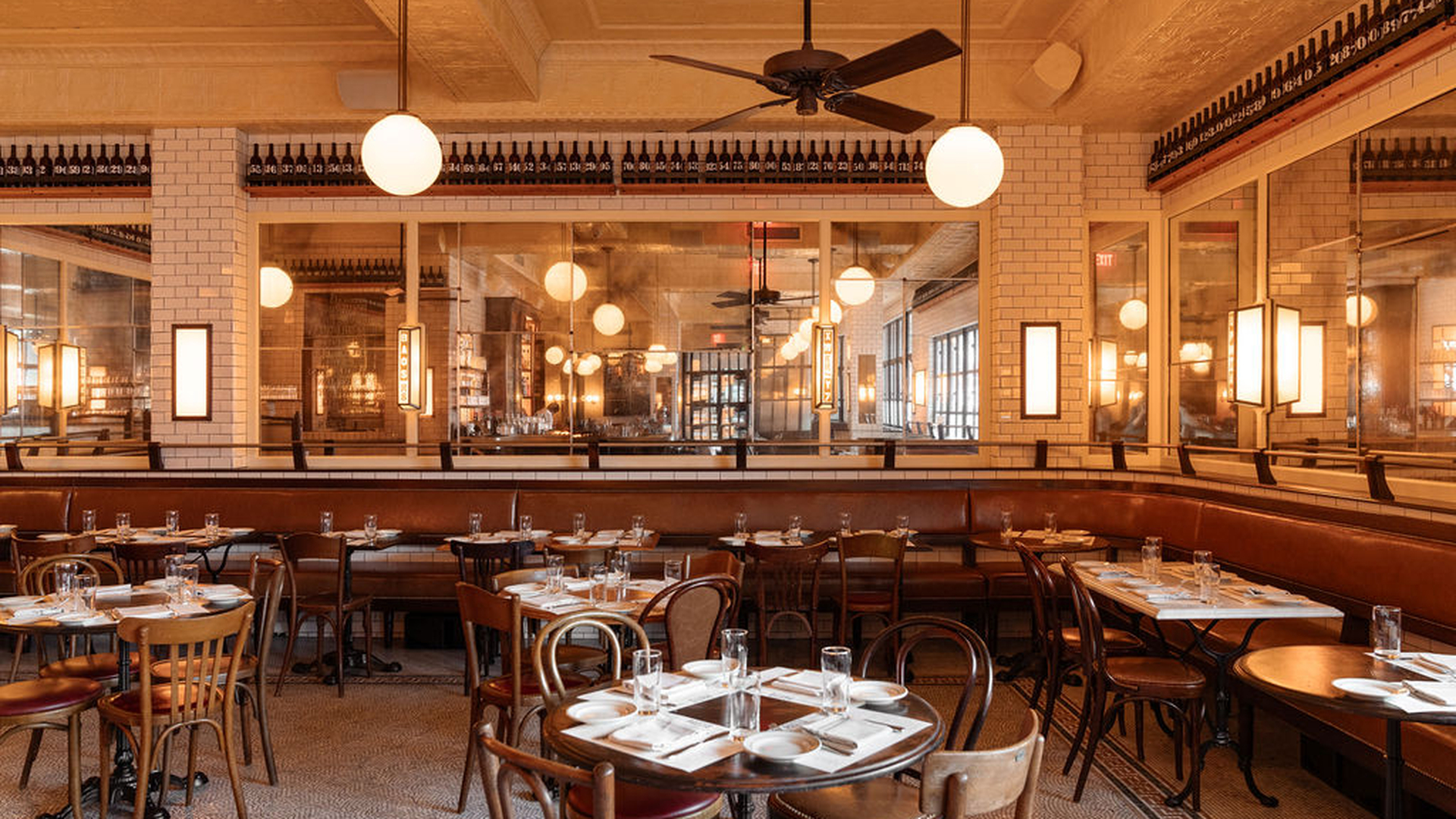 Modern restaurant with wooden tables, glass-paneled walls, and hanging light fixtures, providing a bright and contemporary dining atmosphere.